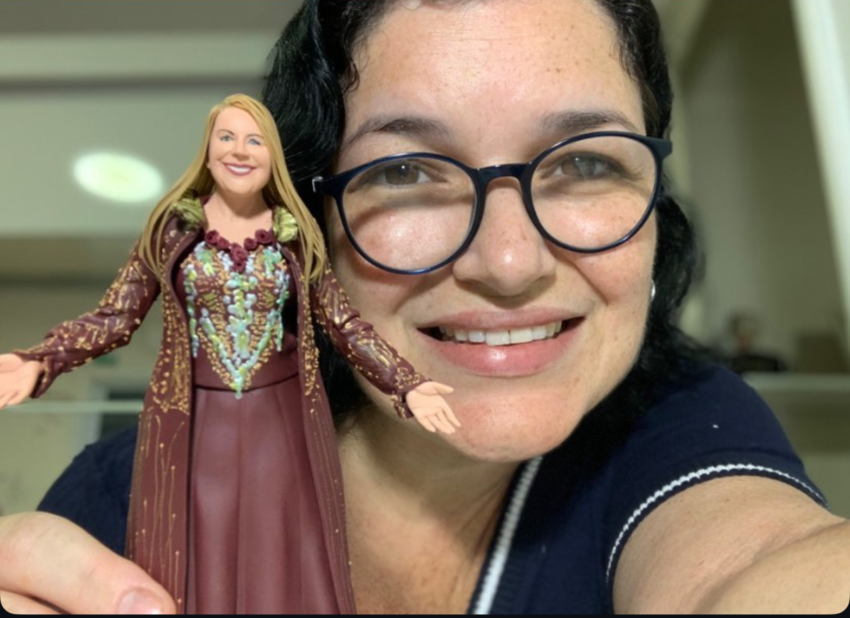 Luzia, jovem artista de 38 anos, sorrindo e segurando uma escultura em miniatura de uma mulher loira com vestido ornamentado, demonstrando sua habilidade artística